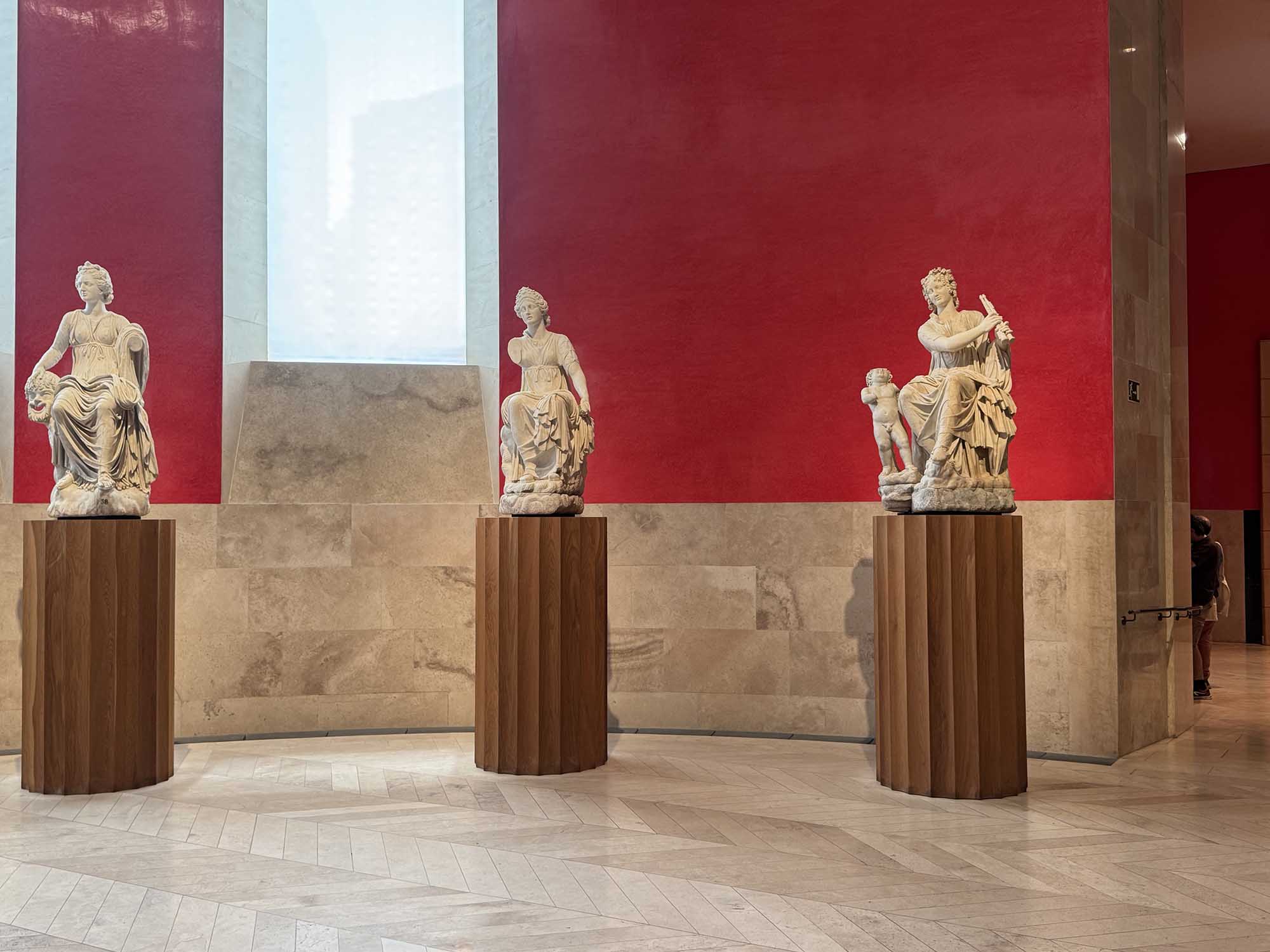 Recovered photo of classical statues displayed in a red-walled gallery at a museum in Madrid.